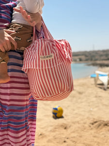 Load image into Gallery viewer, Person holding a red and white striped stroller basket bag on a beach
