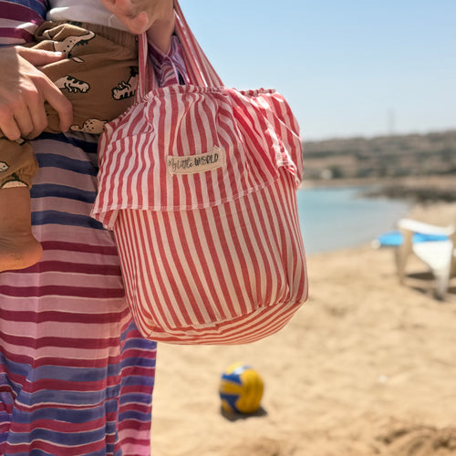 Person holding a red and white striped stroller basket bag on a beach
